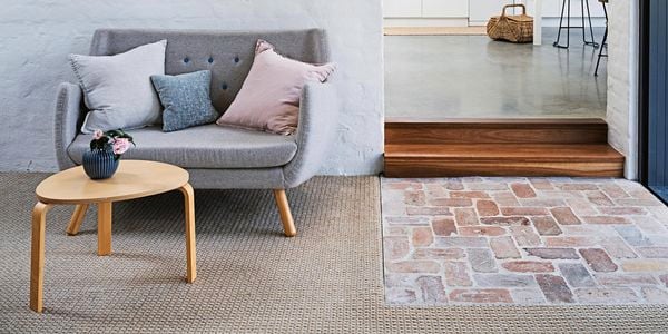 <p>Living room with white brick wall, grey couch, timber coffee table and carpeted floors.</p>
