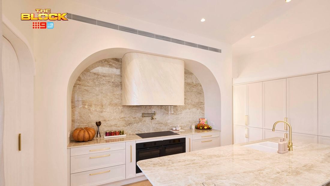 Modern kitchen from The Block with marble island, arched cooking nook, white cabinetry, and stone backsplash.