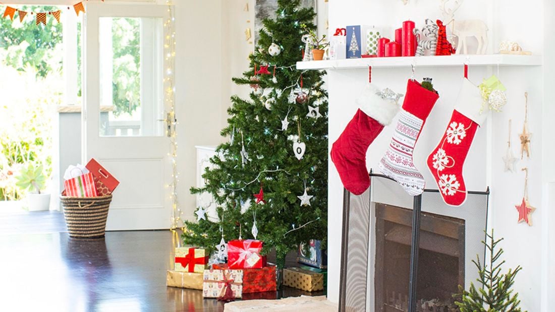 Living room decorated with a Christmas tree, bunting, fairy lights and stockings hanging over a fireplace