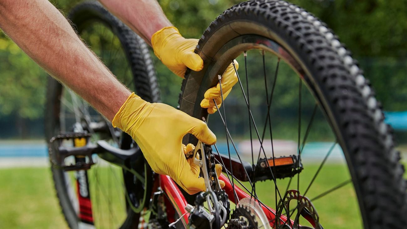 Hands in yellow gloves holds spokes in bike wheel