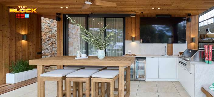 Covered outdoor kitchen and entertaining area featuring a timber bar table, stools, barbecue and timber-lined walls and ceiling.