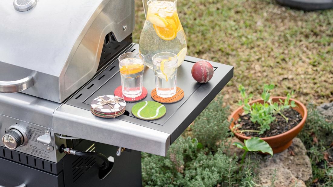 Two drinks placed on coasters which resemble ball sports, sitting on a BBQ's sidetable 