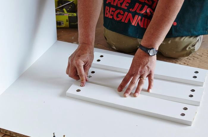 A person attaching rails to the side panel of a cabinet