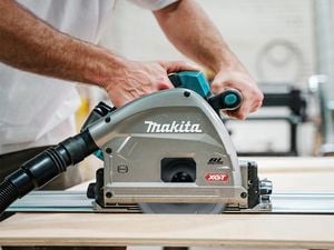 Person using a Makita circular saw with BL motor and XGT label to cut wood along a metal track.
