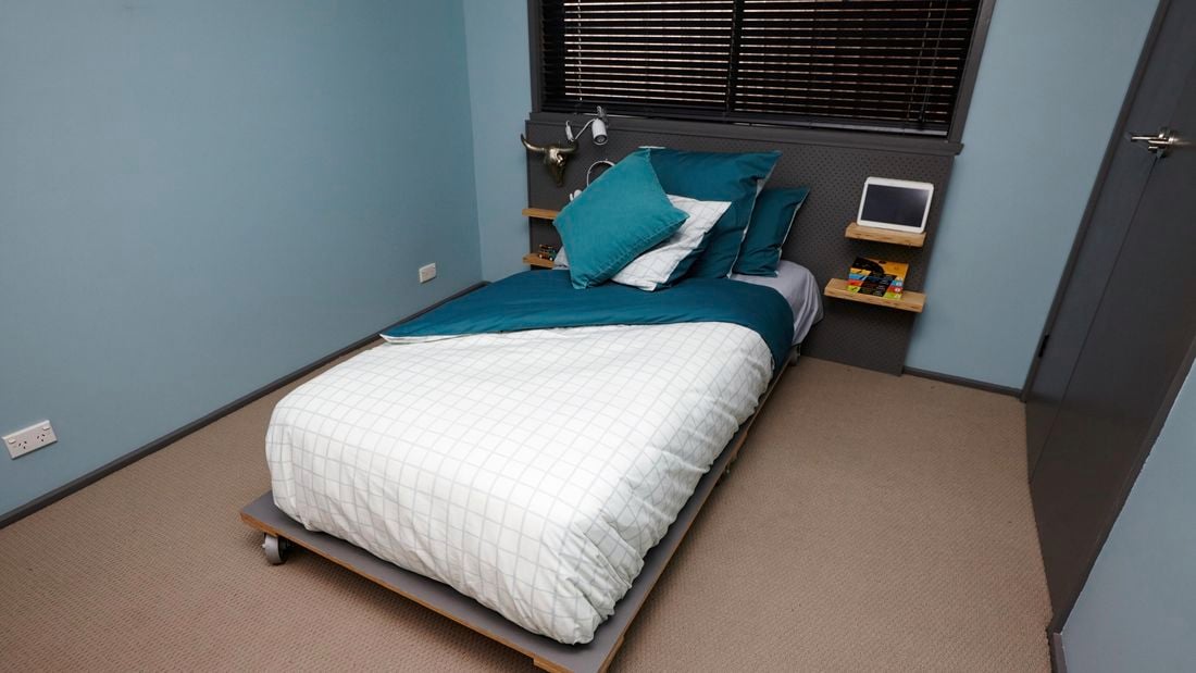 A completed wooden bed frame on wheels, with a made bed in a teal themed bedroom