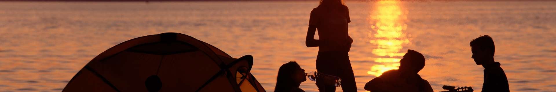 Three people sitting next to a small tent on the beach at sunset