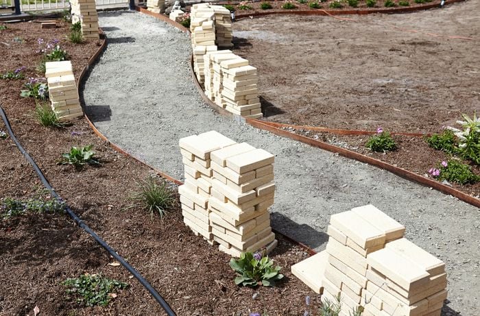 Pavers stacked up on either side of a curved pathway with crushed rock base and edging