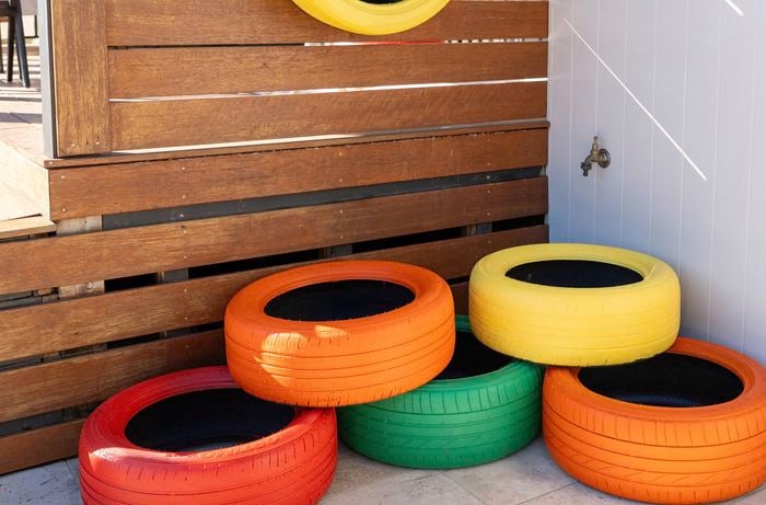 A collection of recycled tyres painted in bright colours including red, orange, yellow and green, stacked together outside.