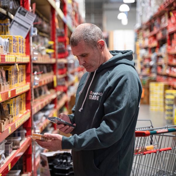 A man in a Bunnings Trade hoodie scans a product on his phone using the Bunnings Trade PowerPass app.