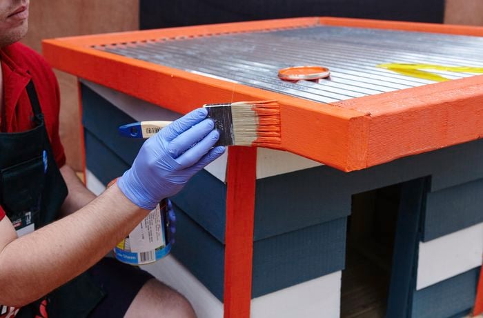 Person painting finished dog kennel with orange paint.