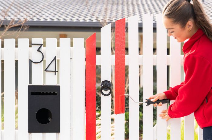 Painting bright red stripes onto a white picket fence gate with a roller.