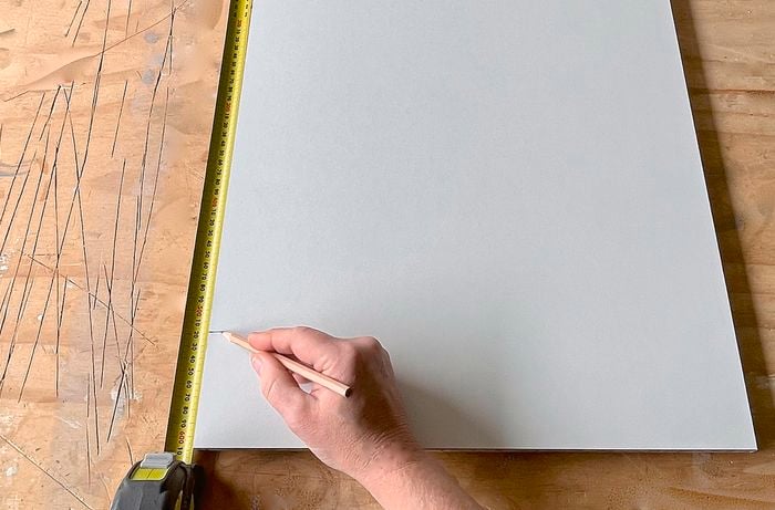 A person measures and marks a cupboard piece with a pencil