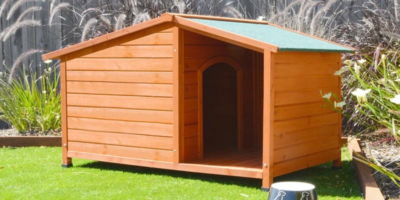 Wooden dog kennel with a green roof and a food bowl at the entrance