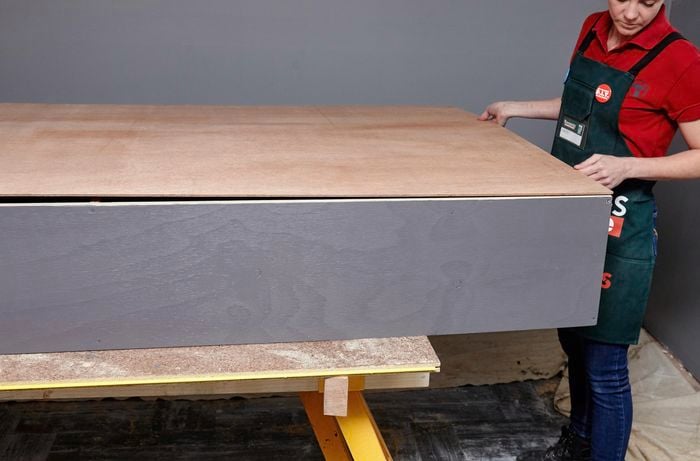 A person fitting a sheet of ply backing onto a shelving unit