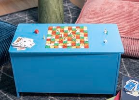 A finished DIY games storage box painted blue with a snakes and ladders board on the lid, styled with dice, playing cards and game pieces.
