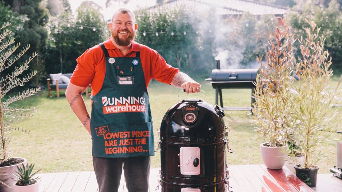 Man standing next to a bullet smoker in a backyard