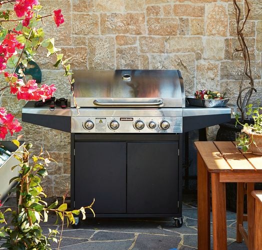 Jumbuck BBQ against a stone brick wall with flowers and plants surrounding