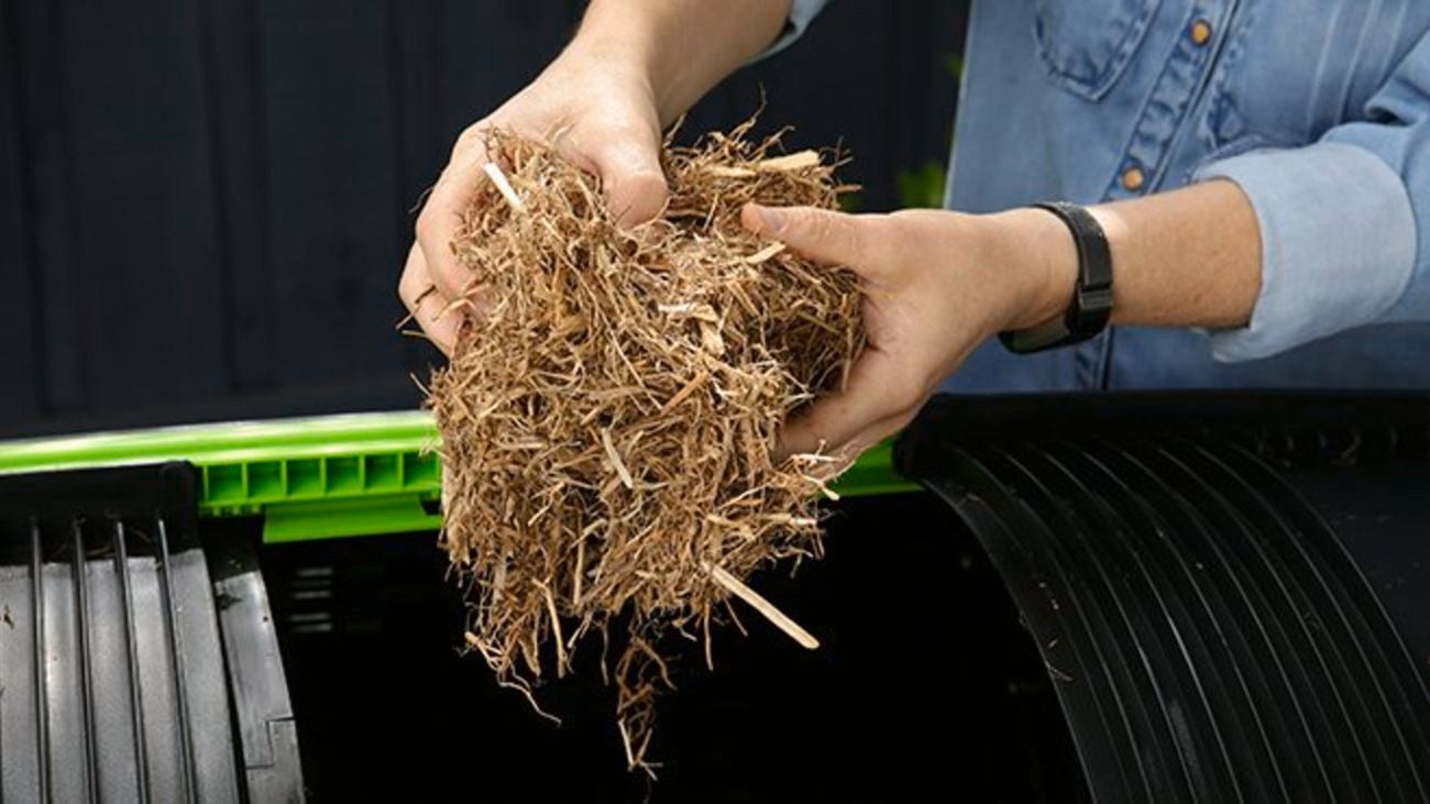 Person holding mulch above compost bin.