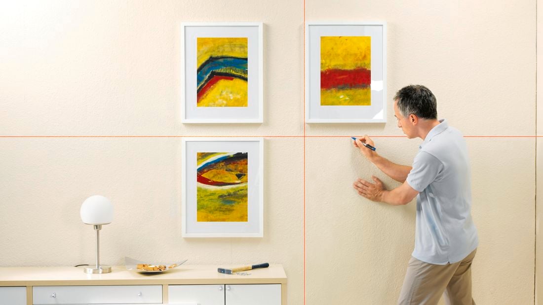 Person using a laser level to hang something up on the wall.