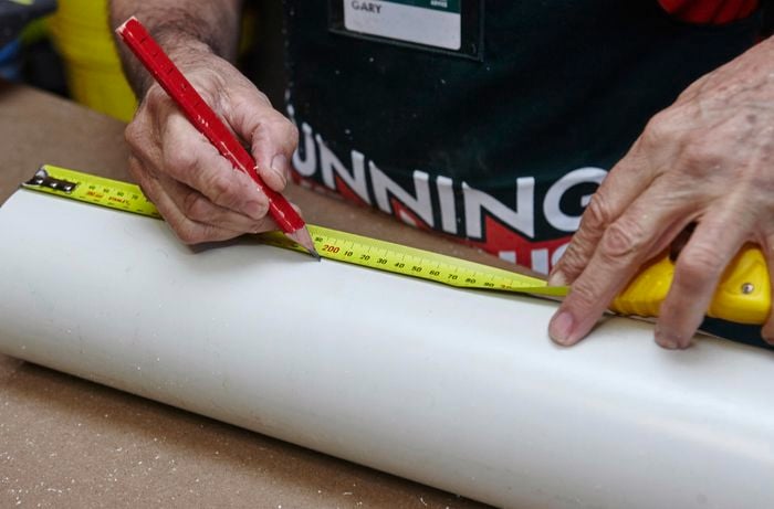 A person marking a measurement on a length of PVC pipe
