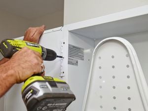 A Bunnings team member using the drill and screws to attach the door to the ironing centre.
