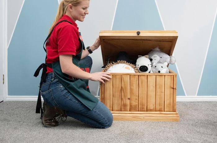 Woman kneeling beside a wooden toybox full of children's toys