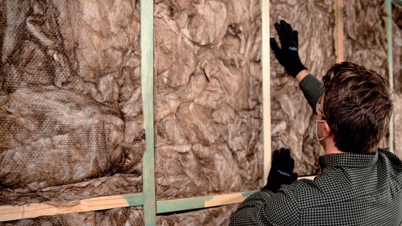 A man wears safety goggles, a mask and gloves while installing insulation.