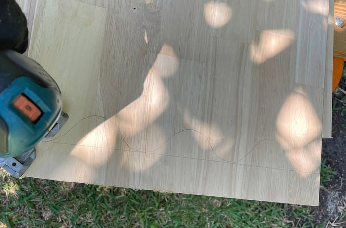 A pine board on sawhorses being cut into a scallop shape with a jigsaw