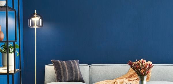 Living room with vibrant blue walls, a wooden coffee table and grey couch behind it, next to a gold floor lamp.