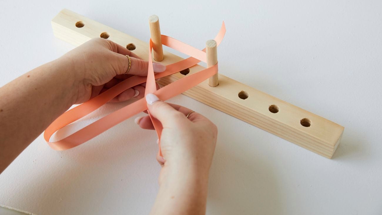 A person using a bow maker to create a bow from peach coloured ribbon.