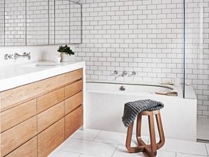 A white themed tiled bathroom with wooden cabinet doors and drawers and wooden bench