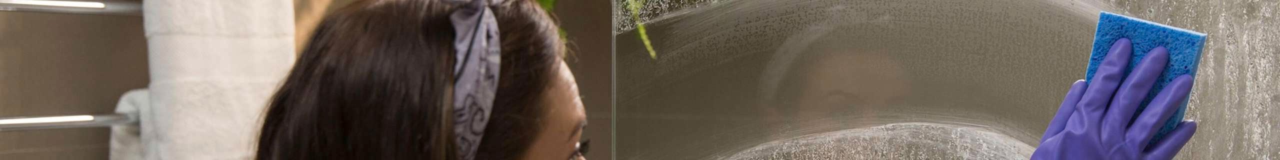 A lady in a bathroom cleaning a shower glass screen.