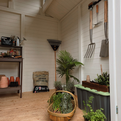 Interior view of a timber garden shed featuring shelving, potted plants, gardening tools, storage containers, and a spacious timber floor.