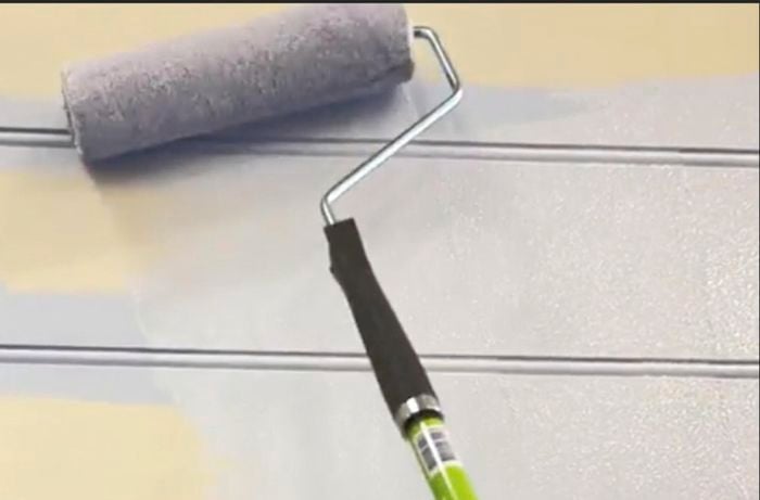 Paint roller applying pastel purple paint to wall.