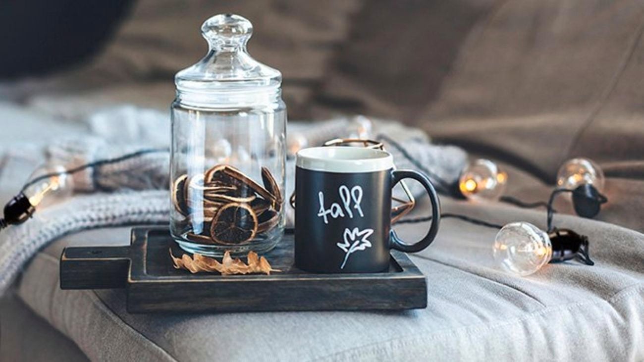 A mug and jar on a board in front of bulb string lights on a couch.