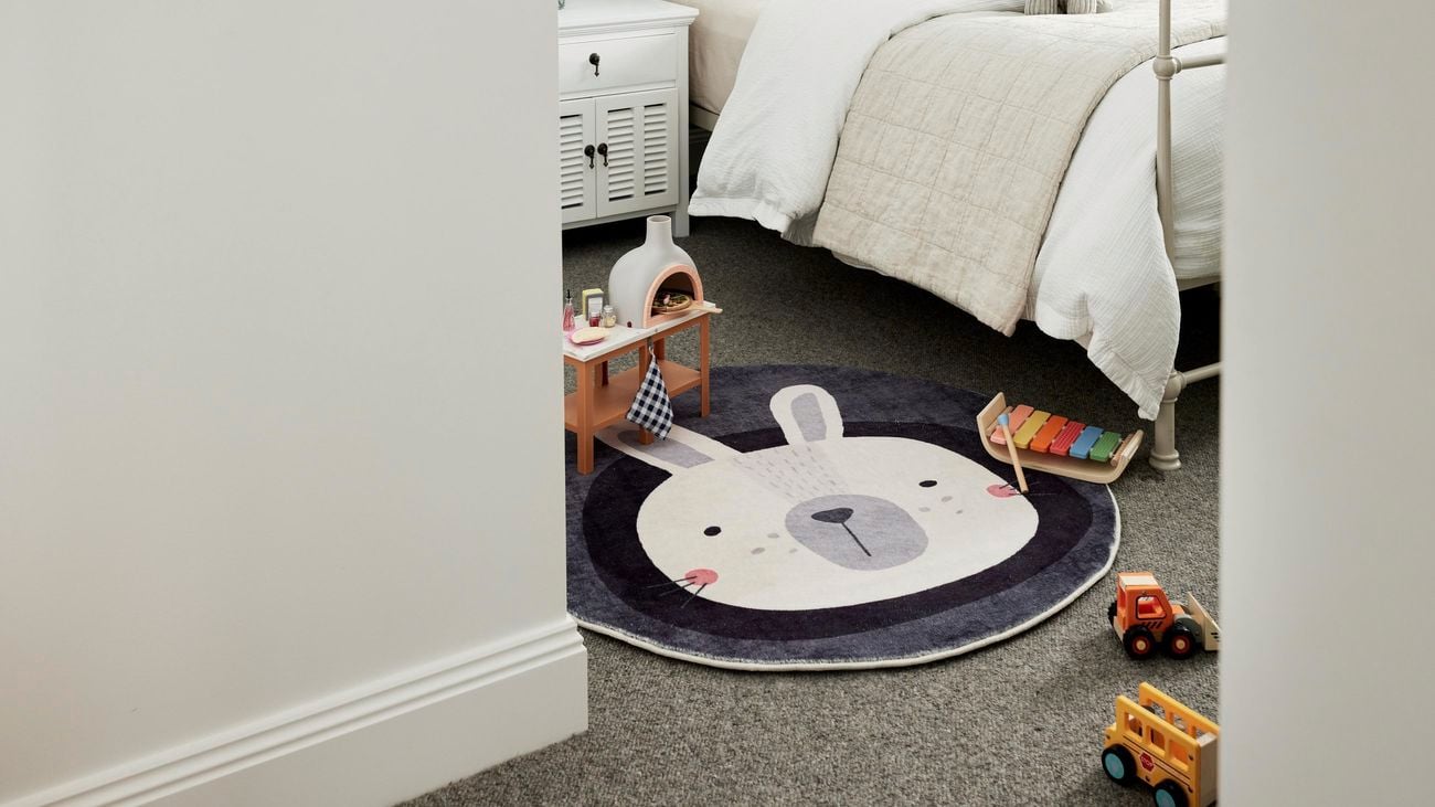 Kids’ room with a bed on top of a rug with a bunny image, surrounded by plastic toys.