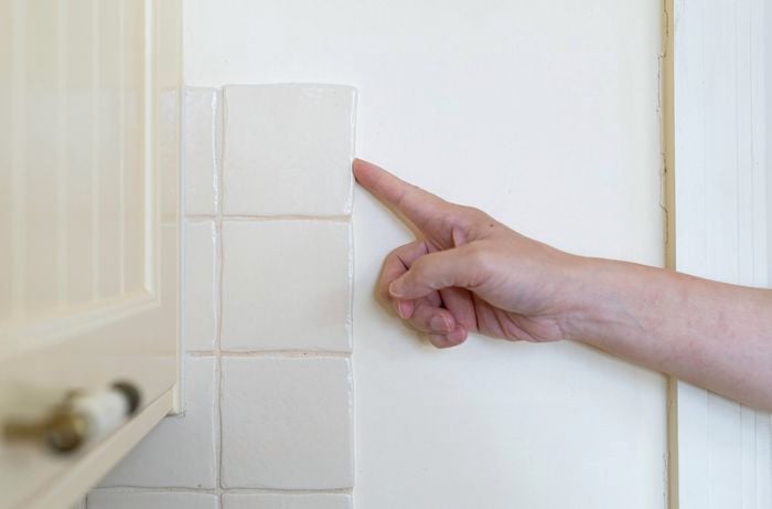 A person pointing to edge tile on wall to select starting point for tile removal