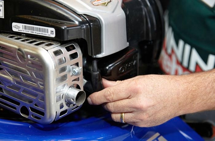A person disconnecting the spark plug on a lawn mower