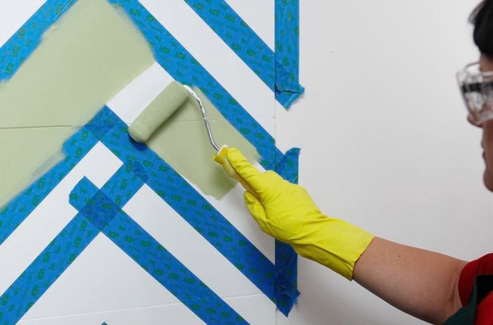 A person using a mini roller to paint tiles masked with masking tape 