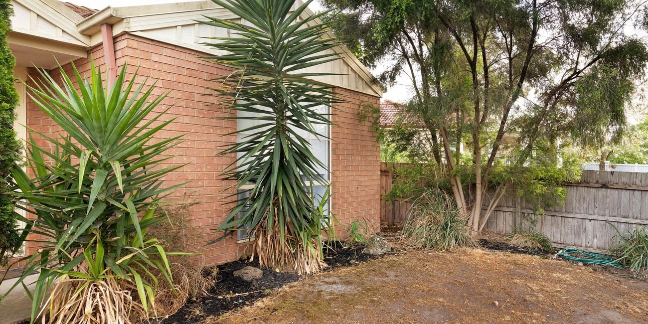 Front of orange brick house, with dirt ground and messy garden.