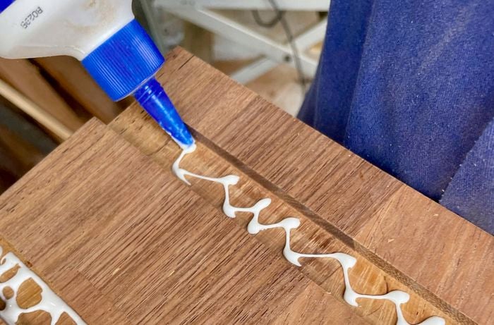 Glue bottle putting white glue into rectangular grooves in wooden planks 