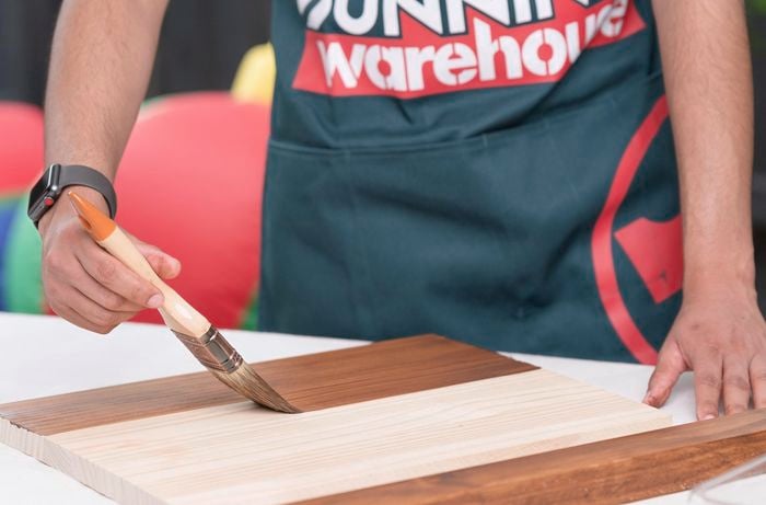 A Bunnings Team Member painting vanish on a piece of wood