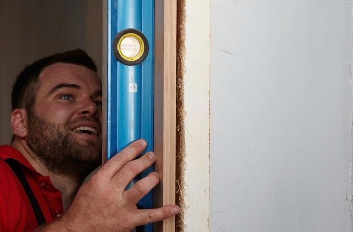 A Bunnings member with a goofy face using a spirit level to check the alignment of a new door jamb