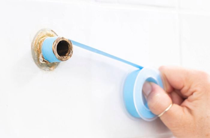 A person is applying plumber's tape to create a watertight seal and help ensure a leak-free shower head installation.