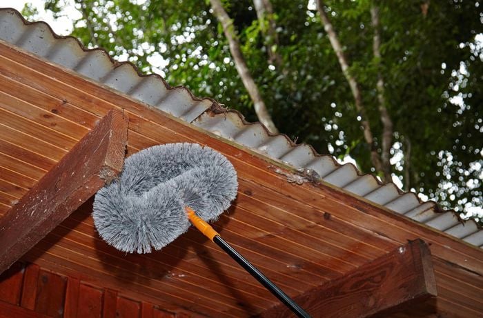 Person cleaning cobwebs from the eaves of a house
