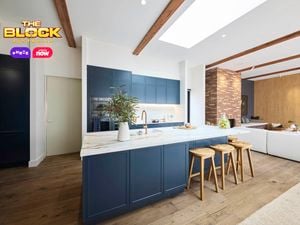 Kitchen with navy island, marble top, wooden stools, and open-plan living.