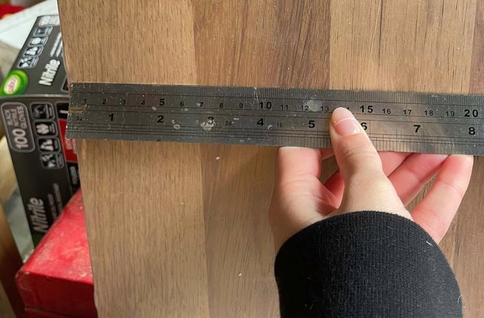 Hand holds a silver ruler horizontally against a plank
