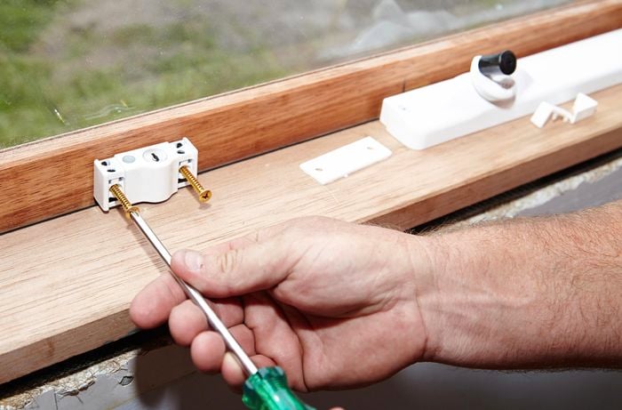 A person attaching a lock to a window using a screwdriver
