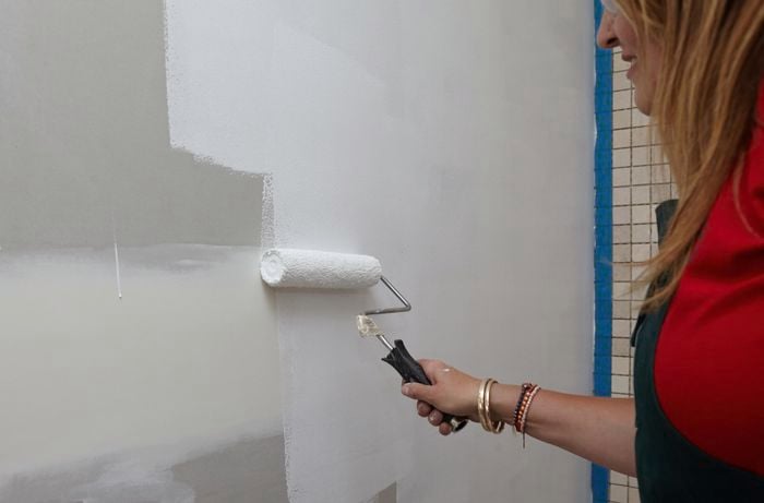 A person painting a plasterboard wall with undercoat using a roller