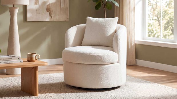 A white chair positioned in a cozy living room, accompanied by a coffee table and a green plant nearby.
